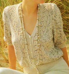 a woman sitting on the ground wearing a sweater and pearls