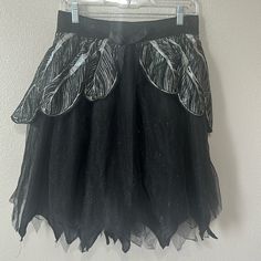 a black tulle skirt with feathers on it hanging from a hanger in front of a white wall