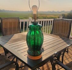 a green glass table lamp sitting on top of a wooden patio table with chairs around it