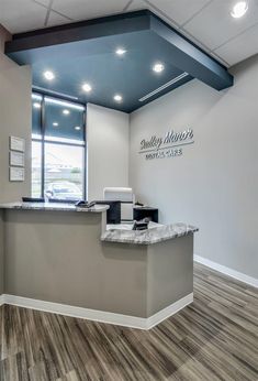 the front desk of a dental office with wood floors and gray walls, along with an open window