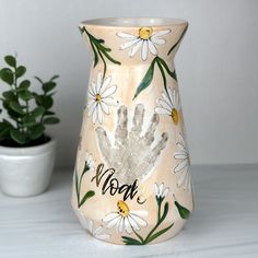 a ceramic vase with handprints on it next to a potted plant