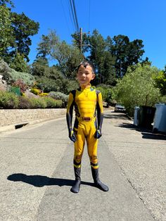 a young boy in a yellow and black diving suit standing on the side of a road