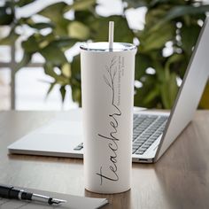 a white tumbler sitting on top of a wooden table next to a laptop