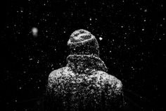 a black and white photo of snow falling on a person's head in the dark