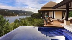 an outdoor swimming pool next to a deck with chairs and tables overlooking the water in front of a house