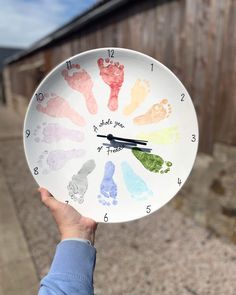 a person holding up a clock with handprints on the front and side of it