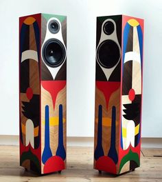 two colorful speakers sitting side by side on a wooden floor in front of a white wall