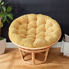 a wicker stool with a round cushion on the floor next to a potted plant