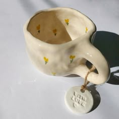 a white ceramic cup with yellow flowers on it and a tag hanging from the handle