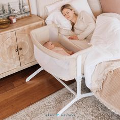 a woman laying in bed next to a baby in a bassinet and changing table