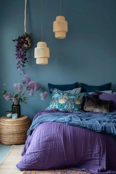 a bedroom with blue walls, purple bedding and flowers hanging from the ceiling above