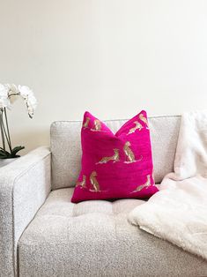 a pink pillow sitting on top of a white couch next to a vase with flowers