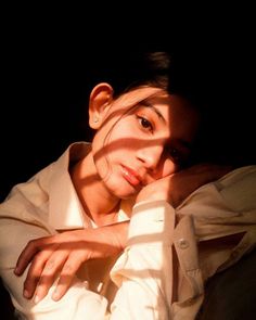 a woman sitting in the dark with her hands on her head and looking at the camera