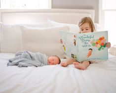 two children are laying on a bed and reading a book to each other while the baby is sleeping next to them