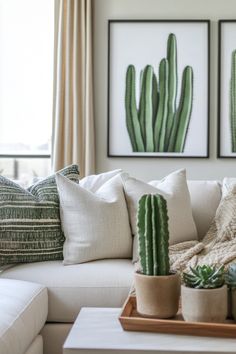 a living room filled with white couches and green cactus art on the wall above them