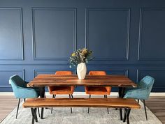 a wooden table with blue chairs and a white vase on top of it in front of a blue wall