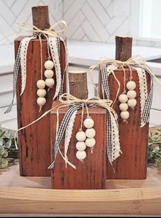 three wooden vases are decorated with white wood beads and twine ribbons on a table