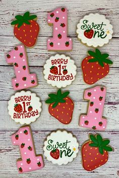 decorated cookies with the number one and strawberrys on them are sitting on a wooden table