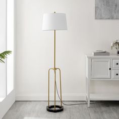 a floor lamp with a white shade on it next to a table and chair in a room