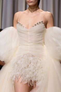 a woman in a white dress with feathers on the skirt and headpieces is walking down the runway