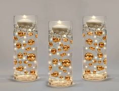 three clear glass vases with gold and white balls on them, one has a lit candle in the middle