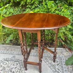 a wooden table sitting on top of a rug in front of bushes and trees with green leaves