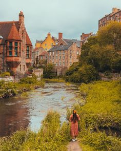 a woman walking down a path next to a river in the middle of a city