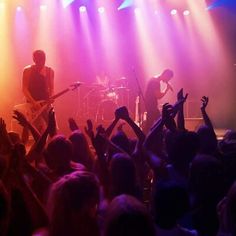 two people on stage with their hands in the air and one person holding up his guitar