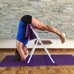 a woman doing a handstand on top of a purple mat in front of a brick wall