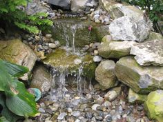 a small garden pond with rocks and water flowing from it's sides to the ground