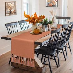 a dining room table with fall decorations on it and an orange runner in the center