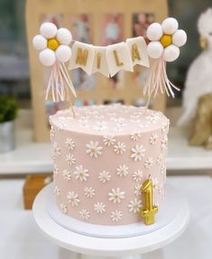 a pink cake decorated with white flowers and balloons