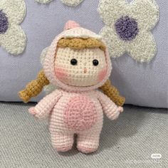 a small crocheted doll sitting on top of a bed next to pillows and flowers