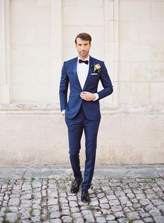 a man in a blue tuxedo and bow tie standing on cobblestone