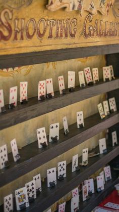 several playing cards are arranged on a shelf in front of a sign that says shooting gallery