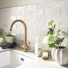 a kitchen sink with flowers and candles on the counter next to it, in front of a white brick wall