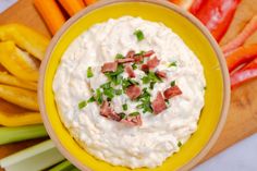 a yellow bowl filled with dip surrounded by carrots, celery and peppers