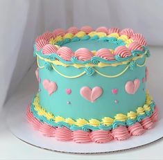 a blue cake with pink, yellow and green frosting hearts on the top is sitting on a white plate