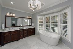 a large white bath tub sitting in a bathroom next to a window covered with blinds