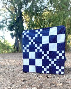 a blue and white quilt sitting on top of a dirt field next to some trees