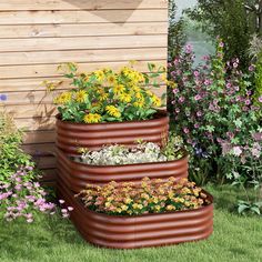 three large planters filled with flowers next to a wooden wall and green grass covered yard