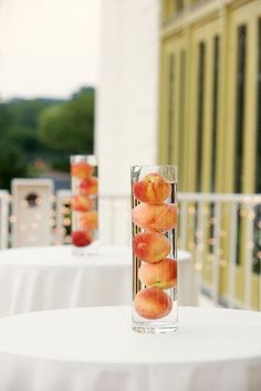 there are four apples in a vase on the table with white linens and lights