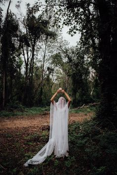 a woman in a white wedding dress standing in the woods with her hands on her head