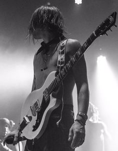 a man with long hair playing an electric guitar in front of two other men on stage