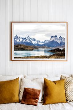 a painting hangs above a bed with white sheets and pillows on it, along with two brown throw pillows