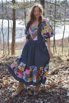 a woman in a dress is standing by some trees and leaves with her hands on her hips