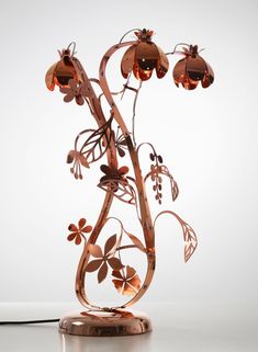 a metal sculpture with flowers and leaves on it's base, against a white background