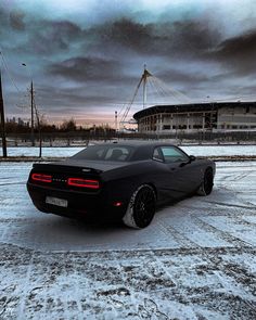 a black sports car parked in the snow near a large building with a sky background