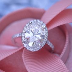 a close up view of a diamond ring on a pink satin ribbon with a blue background