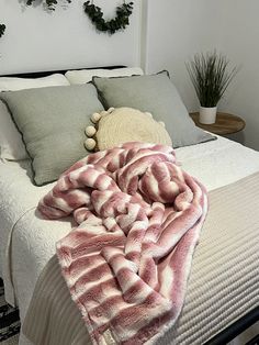 a bed with blankets and pillows on top of it in a bedroom next to potted plants